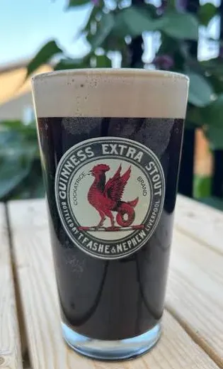 Pint of dark stout displaying a reproduction Guinness Cockatrice Brand label.