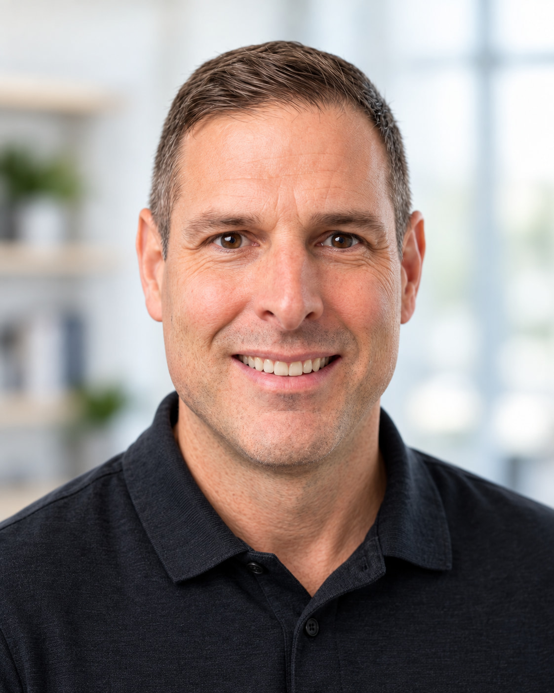 Preferred headshot of Ken Ashe, smiling, in a dark polo shirt